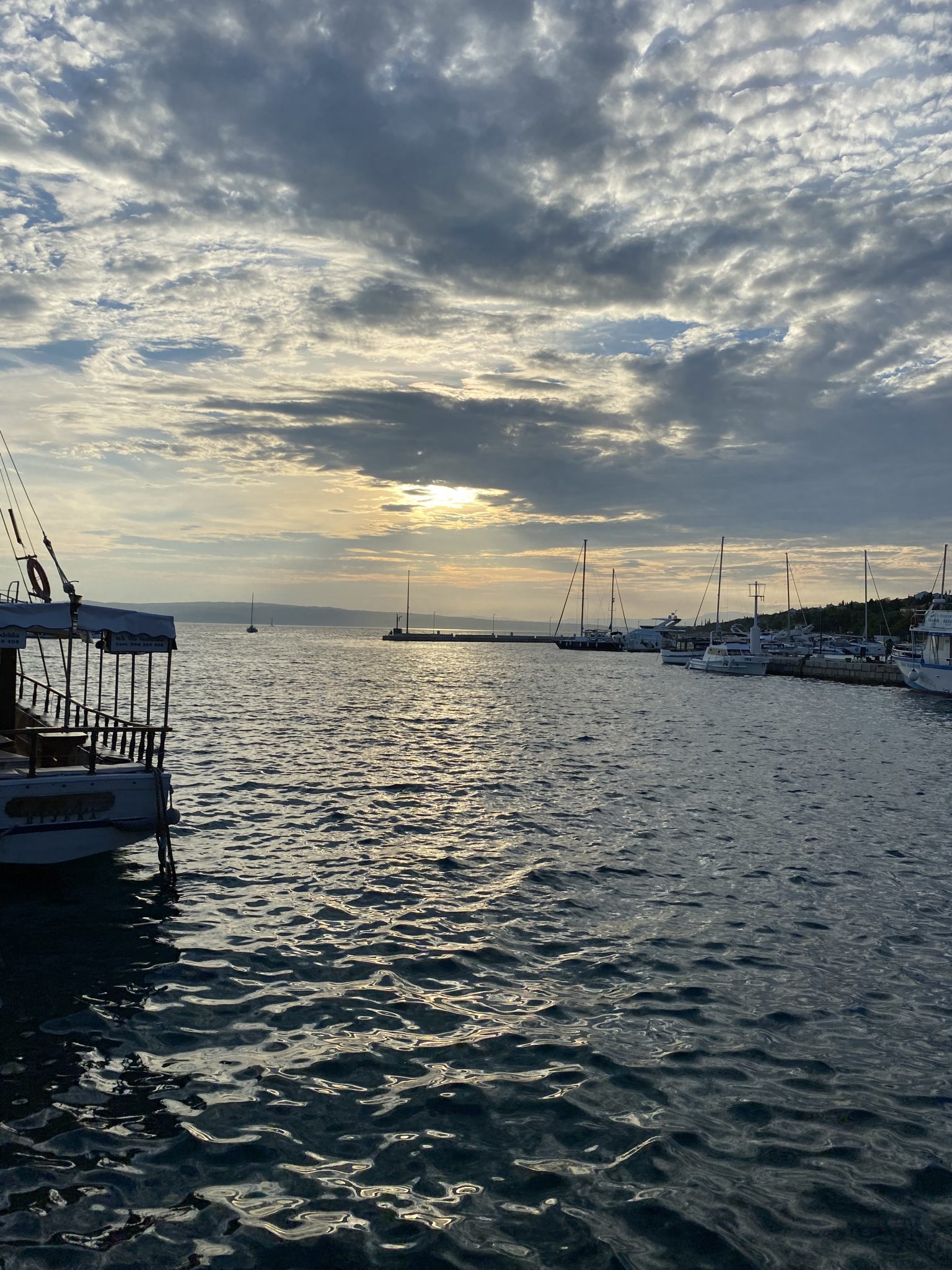 Picture from standing on the bay of marina novi in novi vinodolski looking out on the sea. There is a carpet of clouds with many holes on the sky, the sun is behind the clouds and is soon to set.