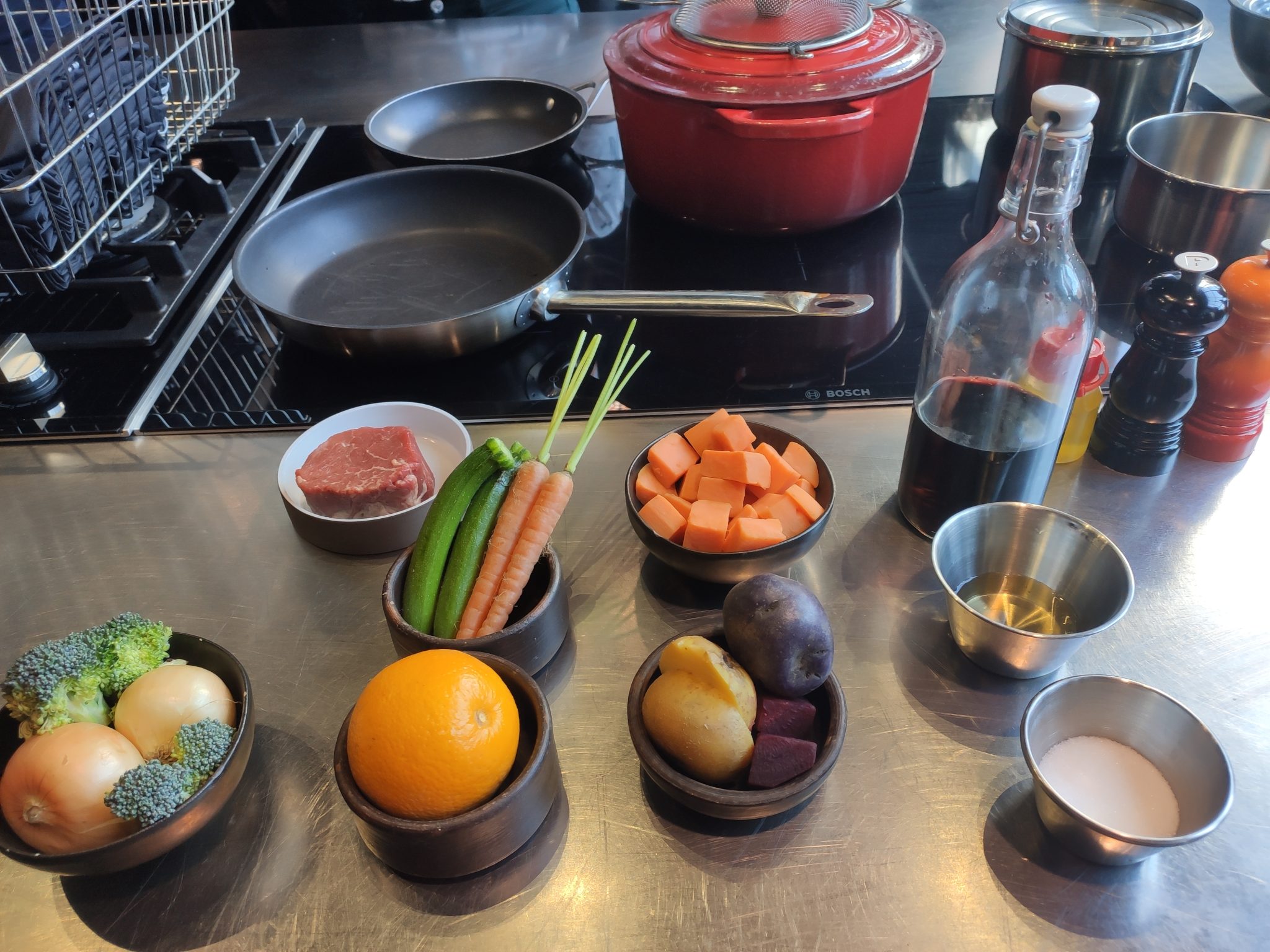 Some kitchen ingredients for a recipe such as orange, onion, potato, meata, carrots, broccoli, red wine, salt and olive oil. Also some kitchenware like two pans (samall and medium size) and a pot