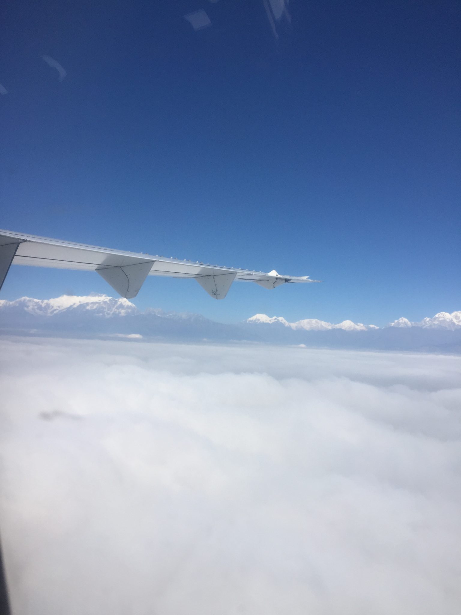 Aeroplane wing, Above the clouds. Very high mountains on the horizon.