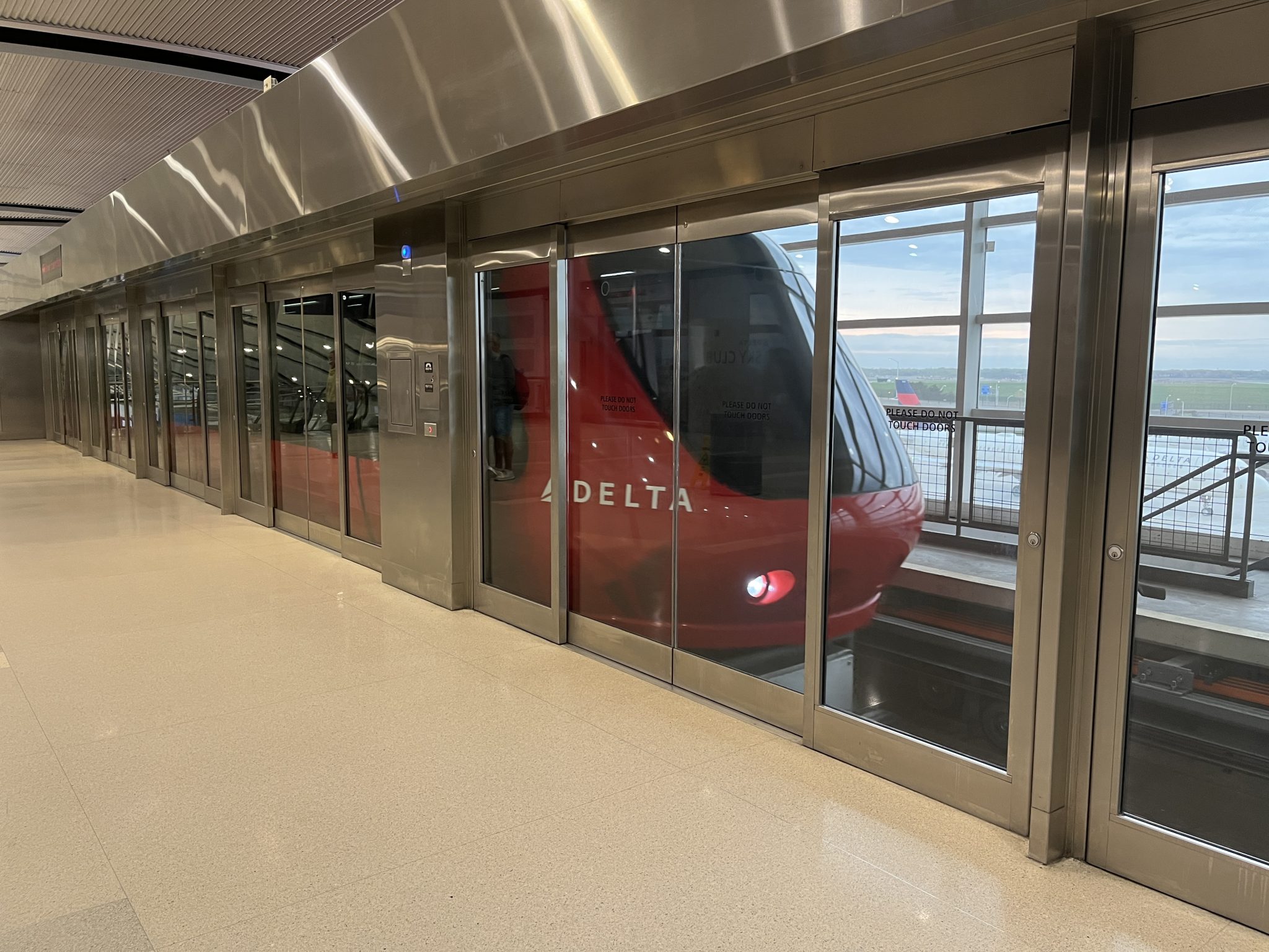 Red commuter train coming into the station inside the Detroit airport. Nose of the train visible through glass doors.
