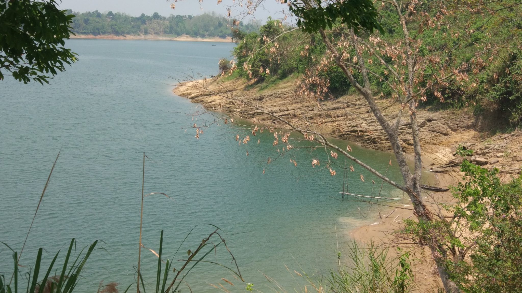 Kaptai Lake side. Sandy shore curing away to the right, small trees along the shore.