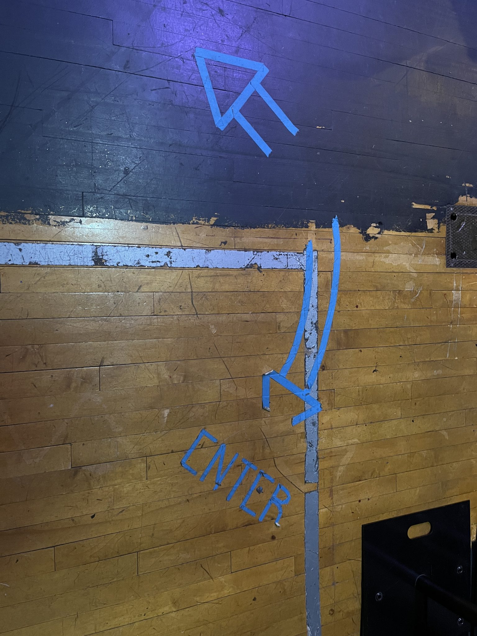 Blue masking tape on a stage floor in the shapes of arrows to direct actors.
