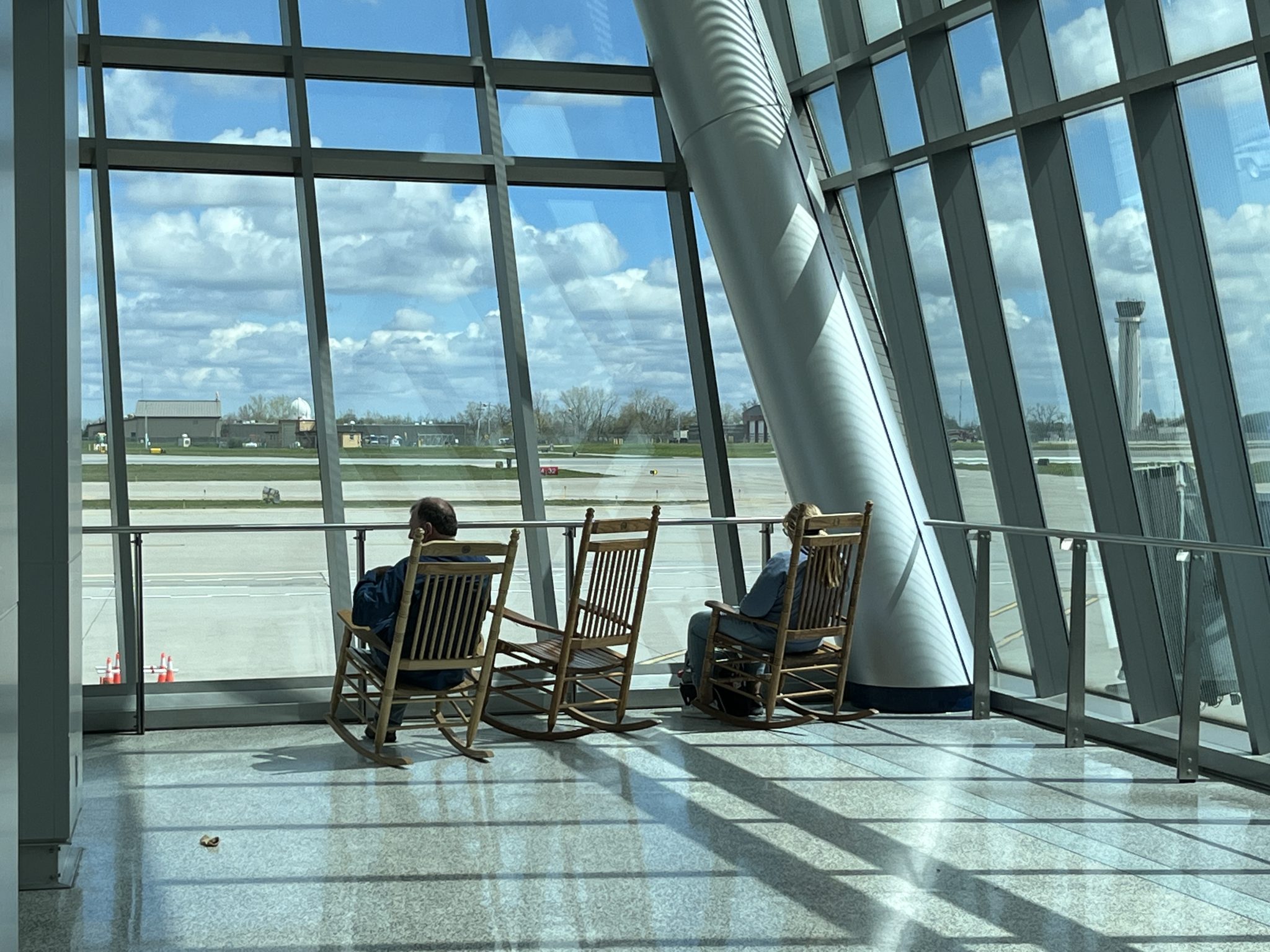 People sitting in rocking chairs in front of giant glass walls at an airport.