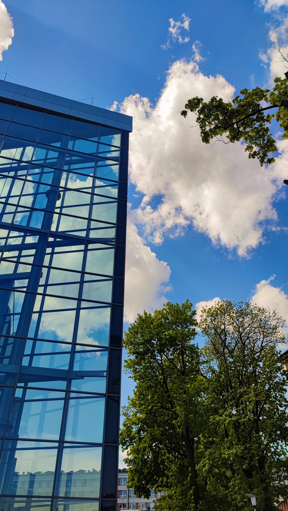 Modern architecture in Gliwice, Poland. Glass and steel building, green trees and blue sky with clouds.