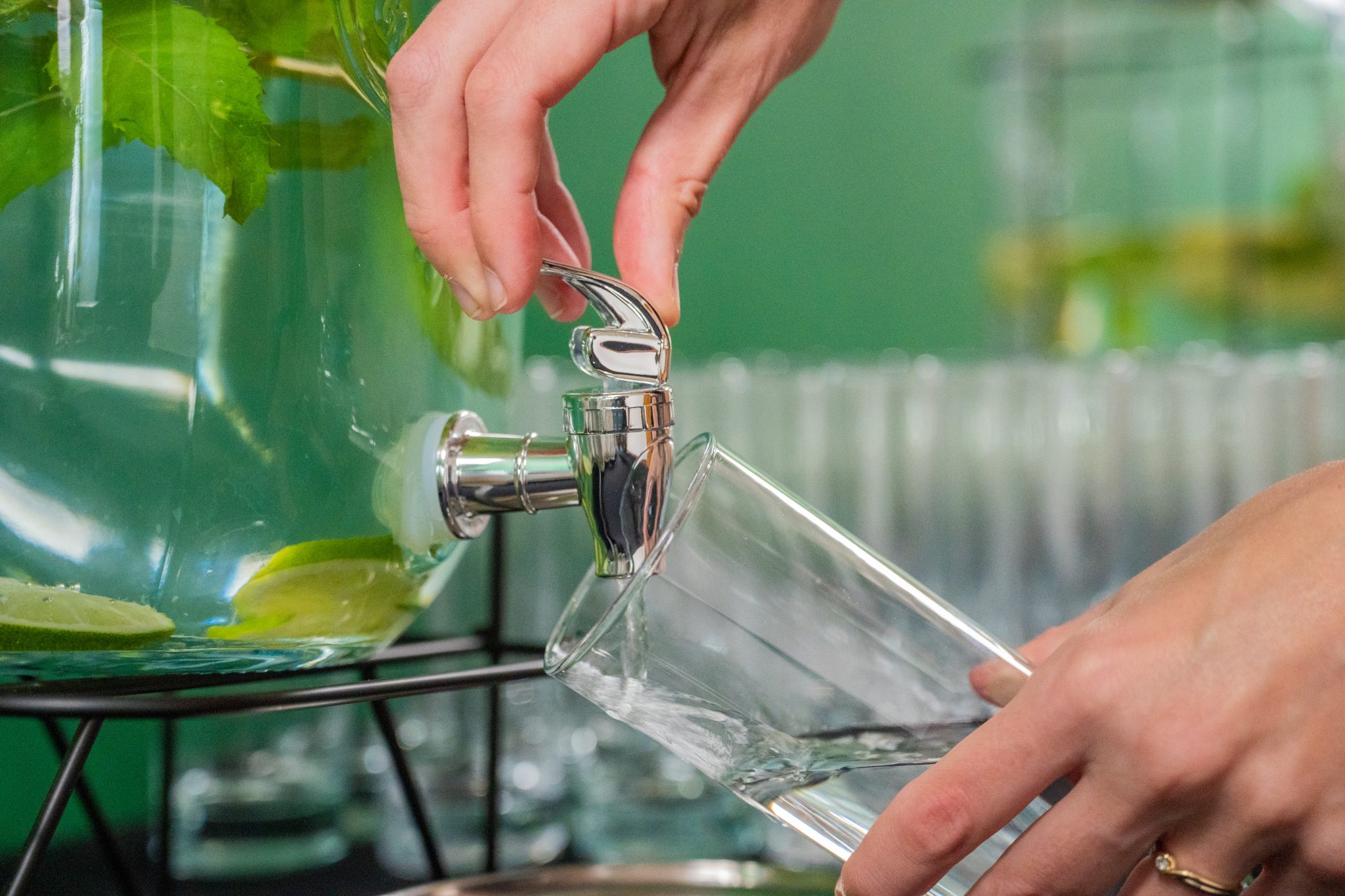 A woman pouring fresh water from a large glass dispenser into a cup