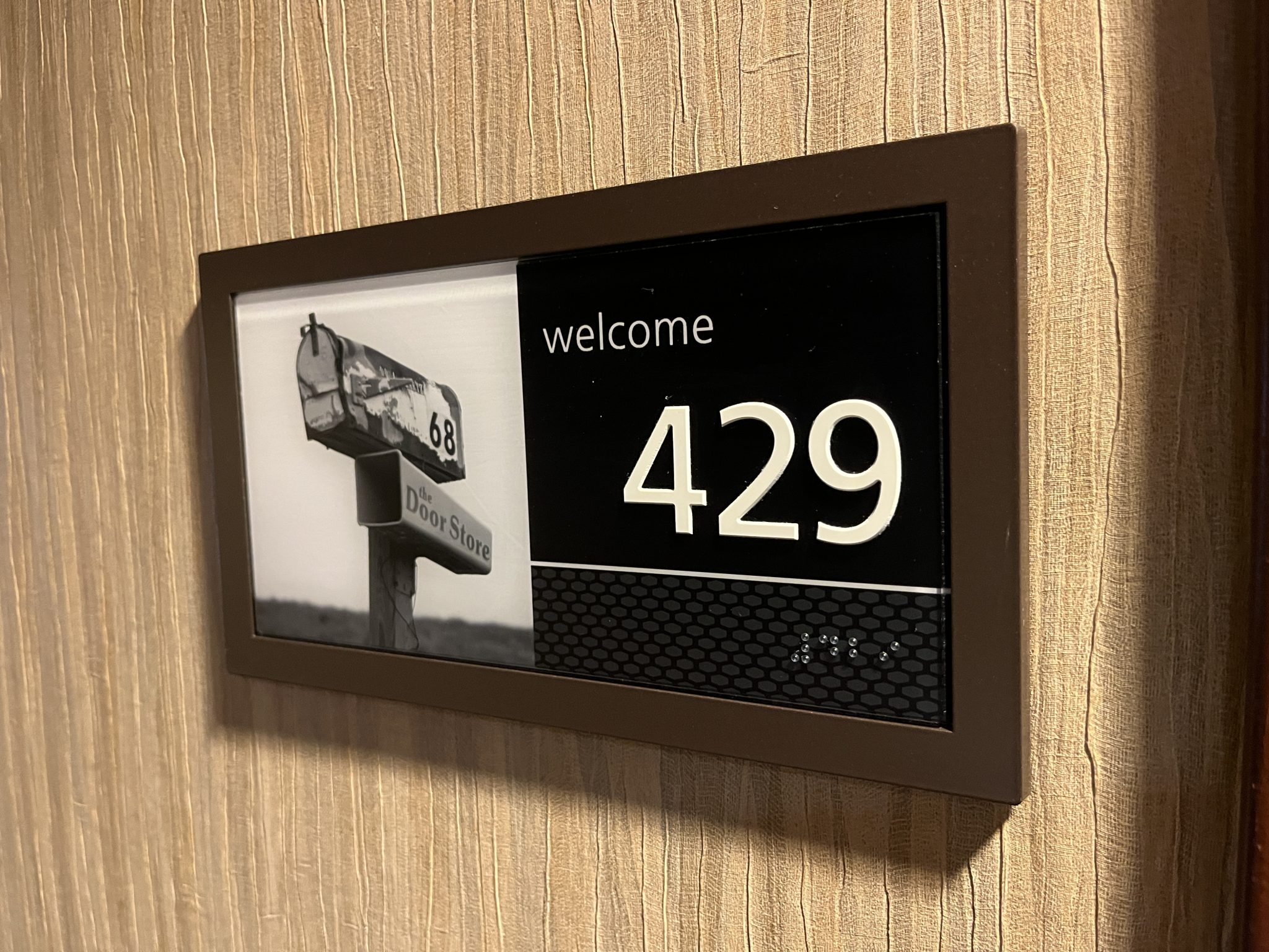 Hotel room door placard. It says Welcome at the top, then room 429. The number is written in braille right under the print, and to the left is a small picture of a mailbox to help people remember their room.