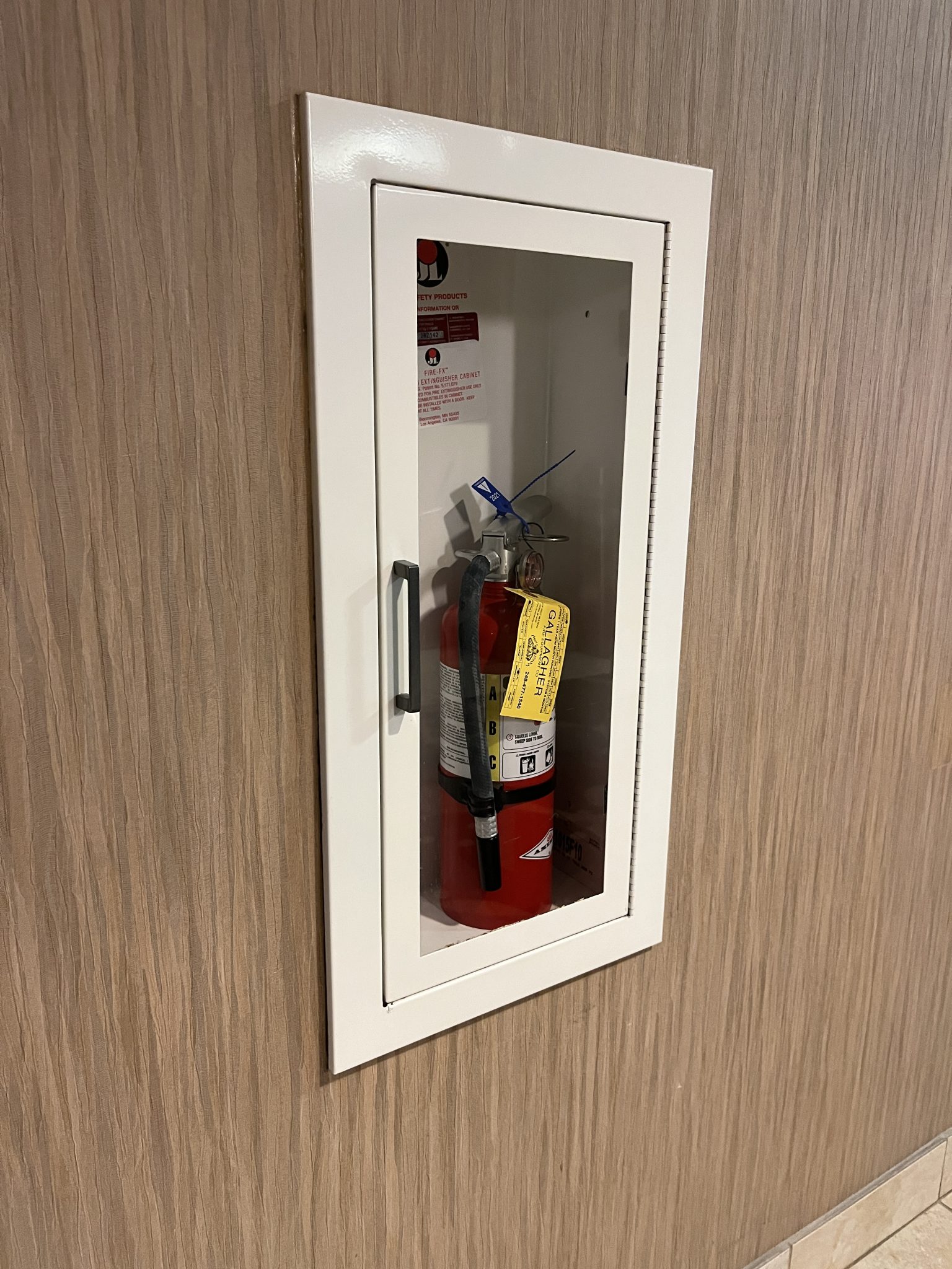 Handheld fire extinguisher in alcove behind glass.