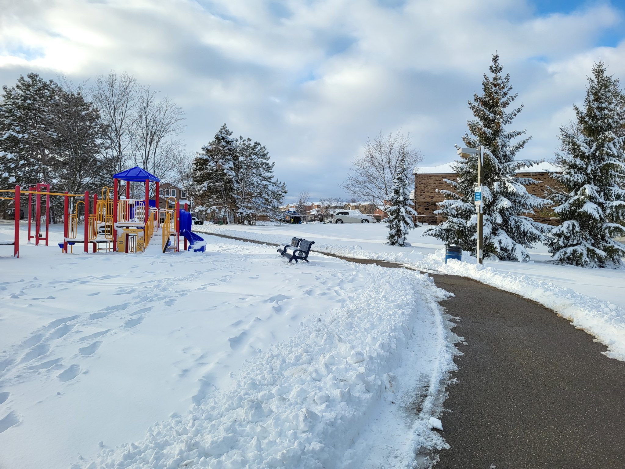 Winter snow along with beautiful nature. Snowy school yard, sidewalk on right curving across to the left behind some playground equipment.
