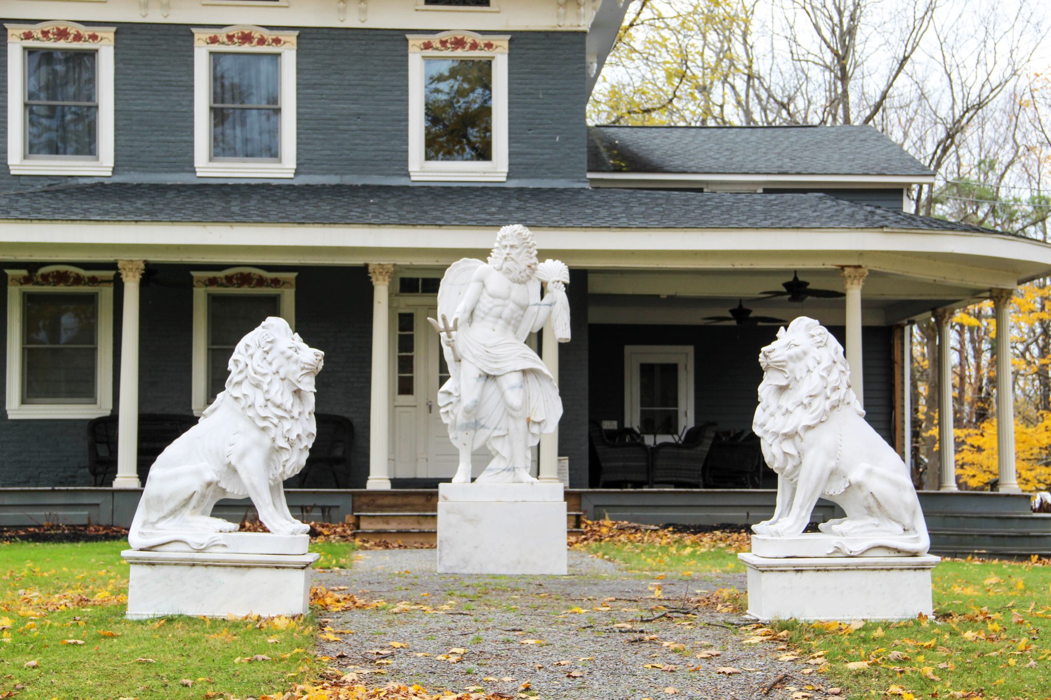 Two lion statues and a statue of Neptune sit in the front yard of a slate blue house in Sodus Point, New York, USA.
