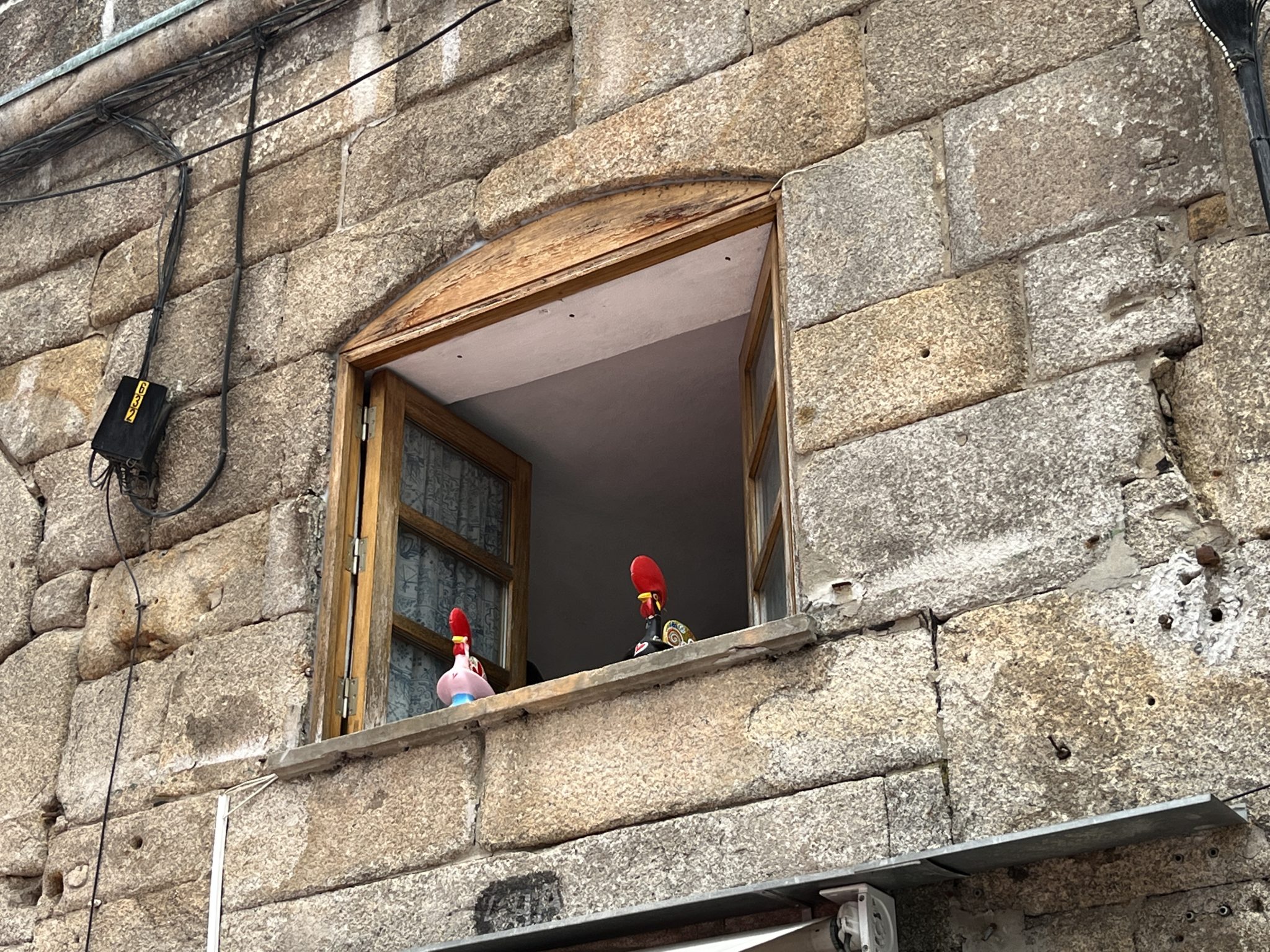 Metal roosters looking out a window in Porto, Portugal