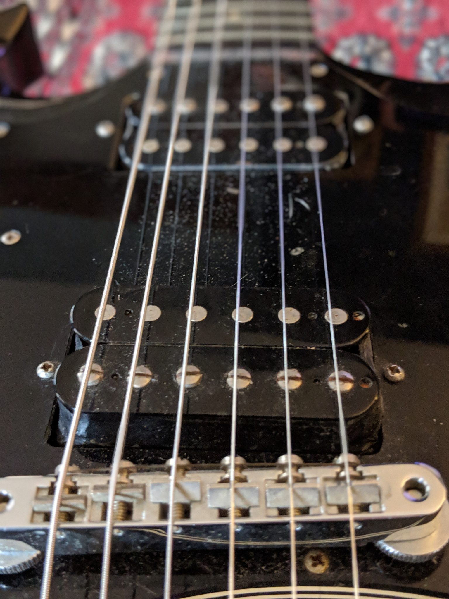 A closeup of a black guitar, overlooking bridge and pickups
