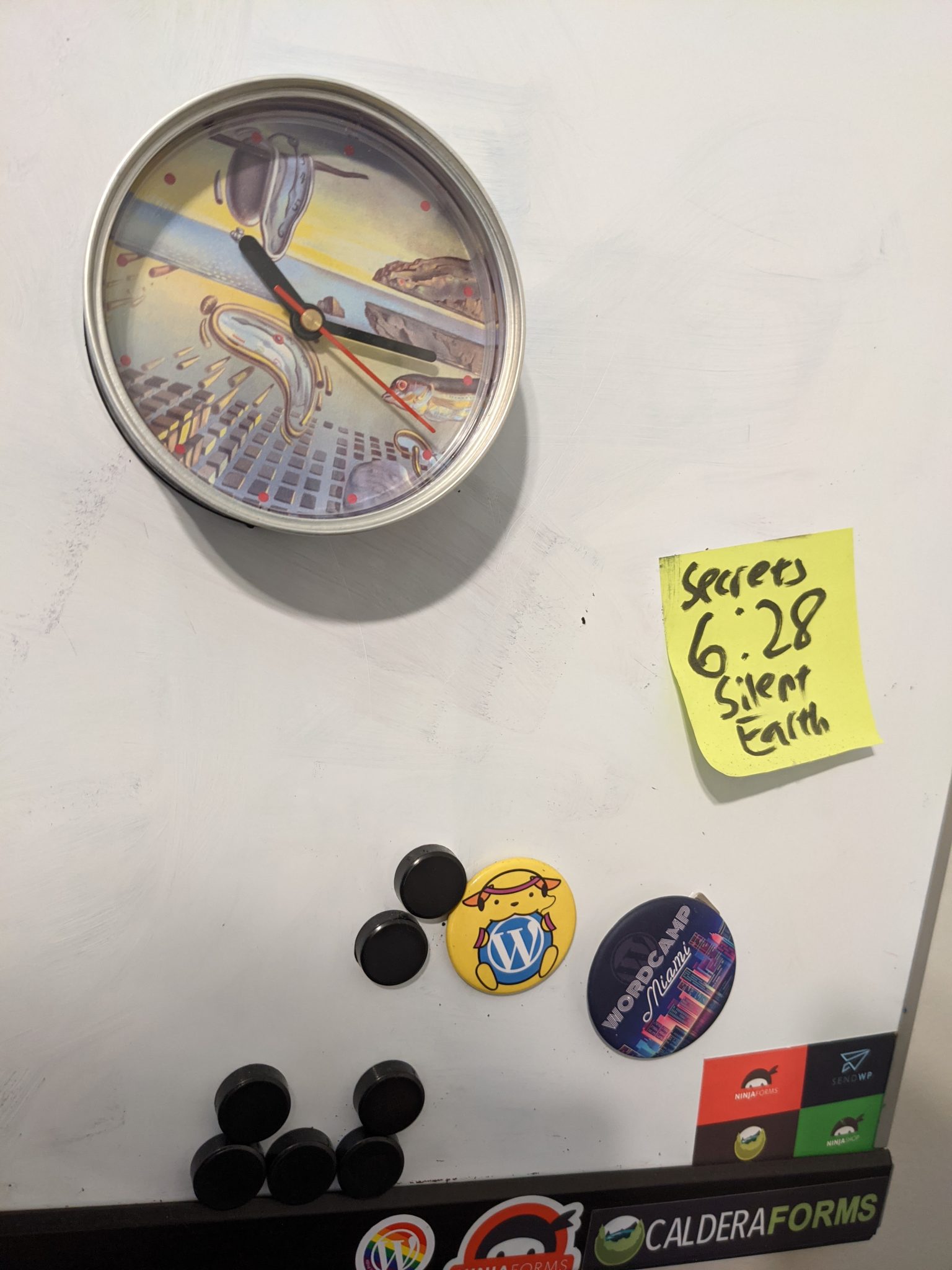 A white board, with several WordPress magnets and a yellow post it note that says "Secret Silent Earth 6:28"
