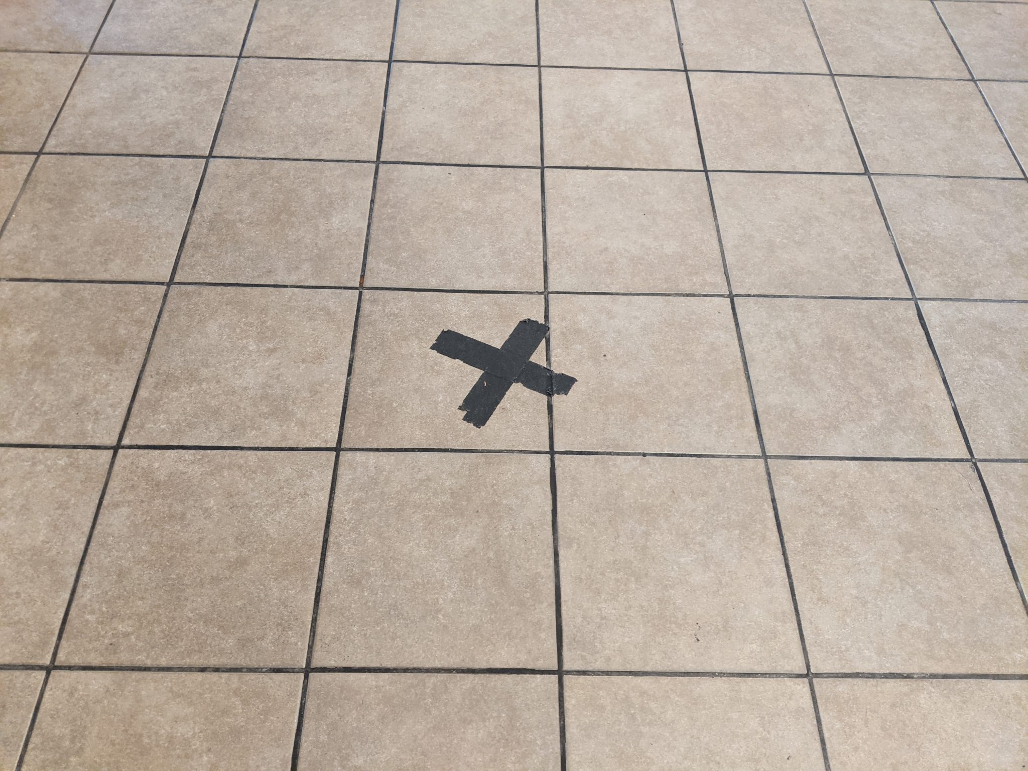 Black tape making an X on the floor to help with social distancing